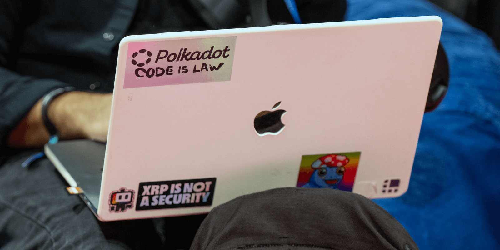 Close-up of a laptop at Consensus 2025, covered in crypto stickers including "Polkadot: Code Is Law" and "XRP is not a security."