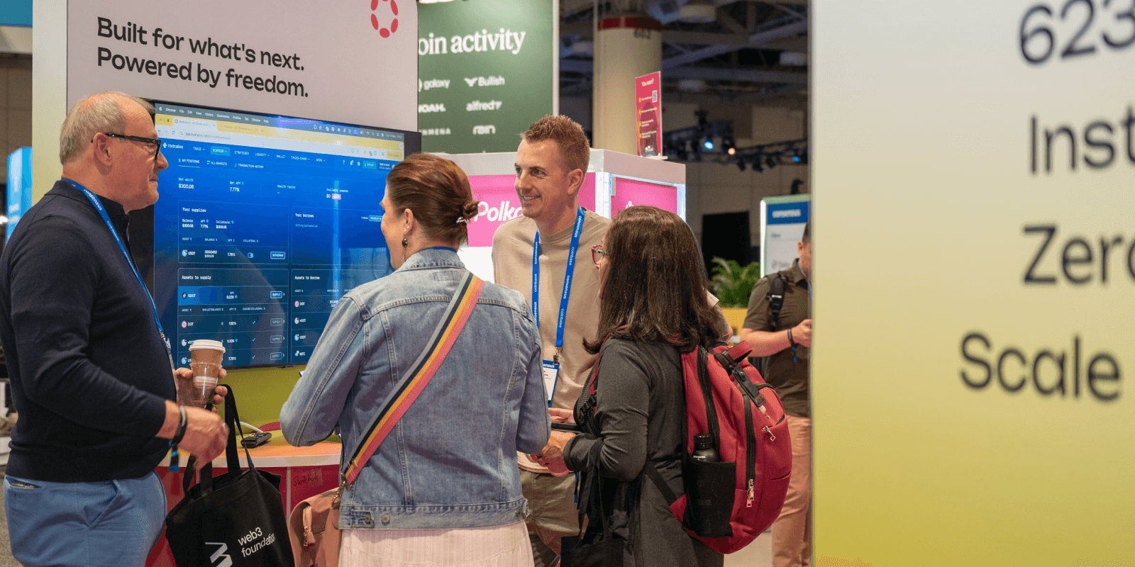 Consensus 2025 attendees gather around the Polkadot demo station, engaging with an on-screen app under the banner "Built for what's next. Powered by freedom."